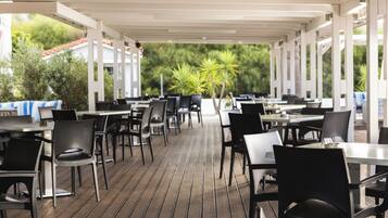 Un espace de restauration en plein air, doté de tables et de chaises, recouvert d’un toit blanc et entouré de verdure.