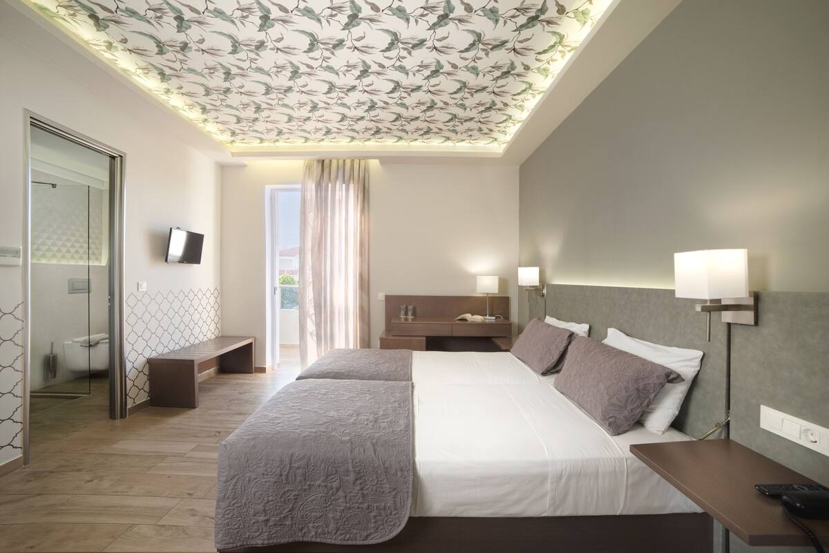 Une chambre d’hôtel moderne dotée d’un grand lit, de tables de chevet, d’un bureau et d’une salle de bain avec une douche en verre.