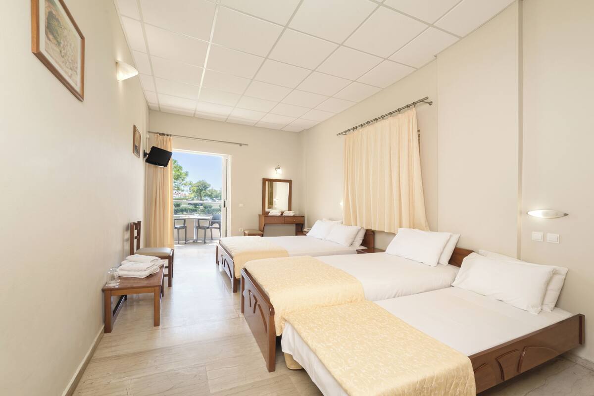 Une chambre d’hôtel avec deux lits, un bureau avec une chaise, une petite table avec des verres et une fenêtre avec des rideaux.