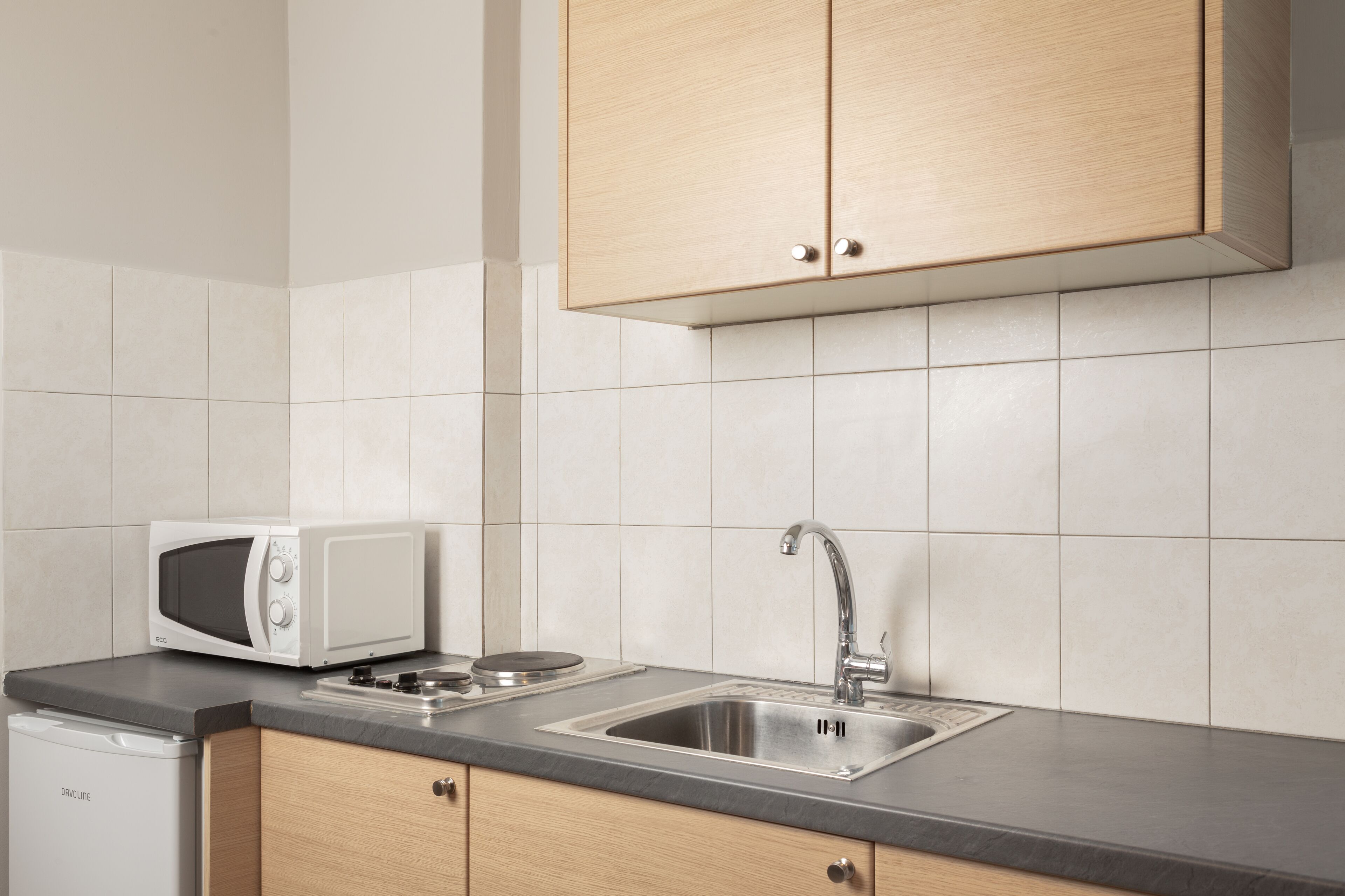 Una cocina con microondas, lavamanos y armarios de madera.
