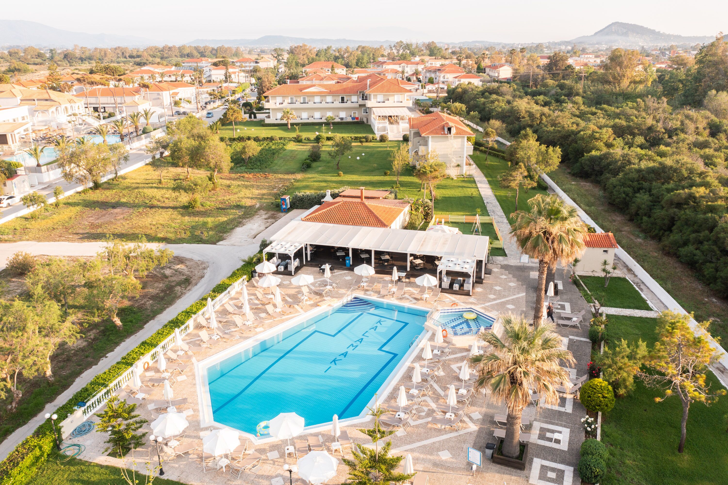 A resort with a large swimming pool, sun loungers, and a covered area with umbrellas.
