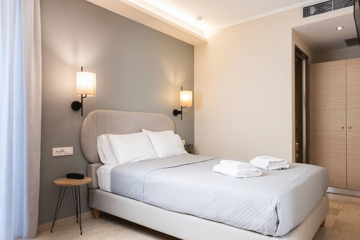 Une chambre moderne avec un grand lit, deux lampes fixées au mur, une petite table de chevet et une armoire.