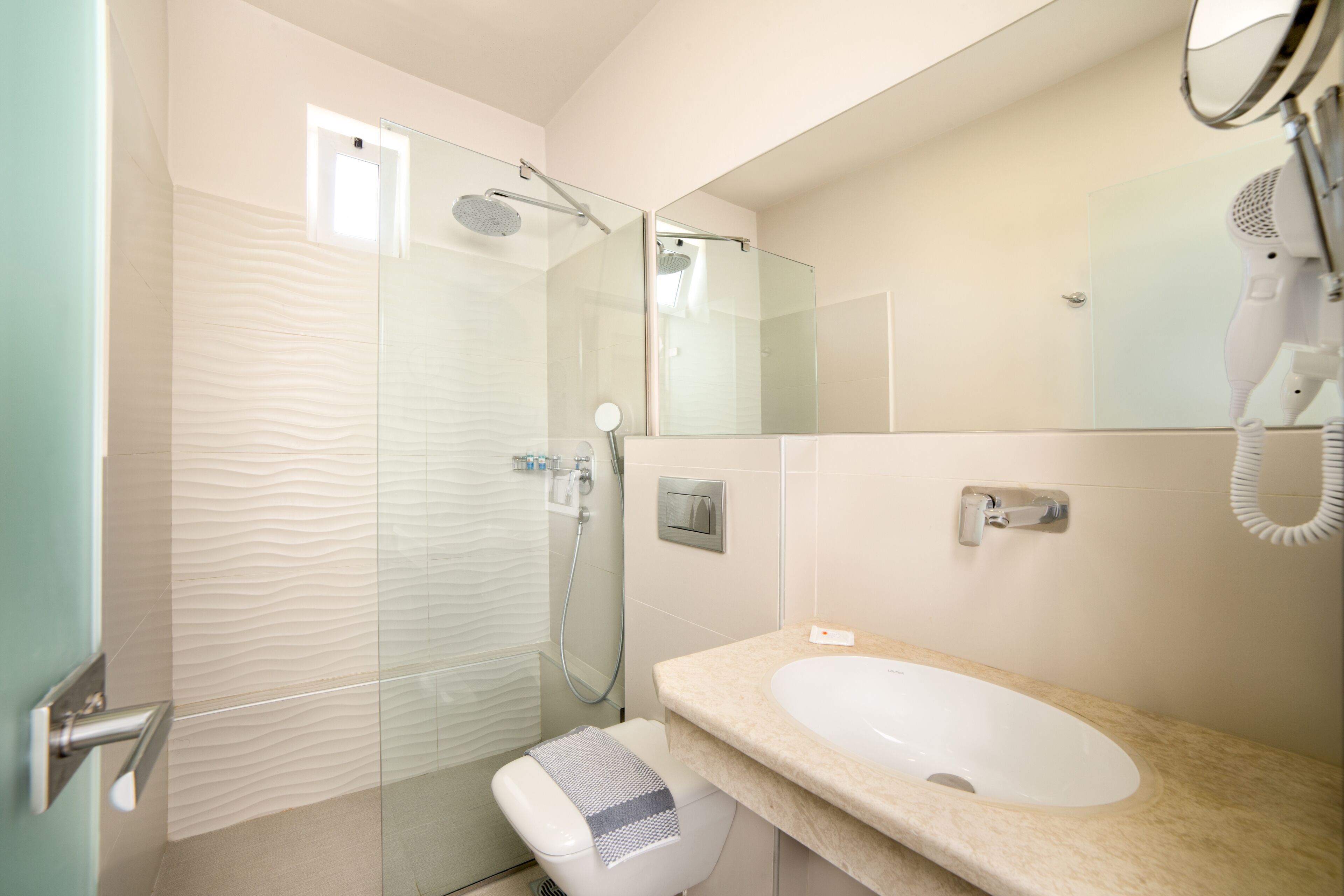 A modern bathroom with a glass shower enclosure, a white sink, and a handheld hair dryer mounted on the wall.