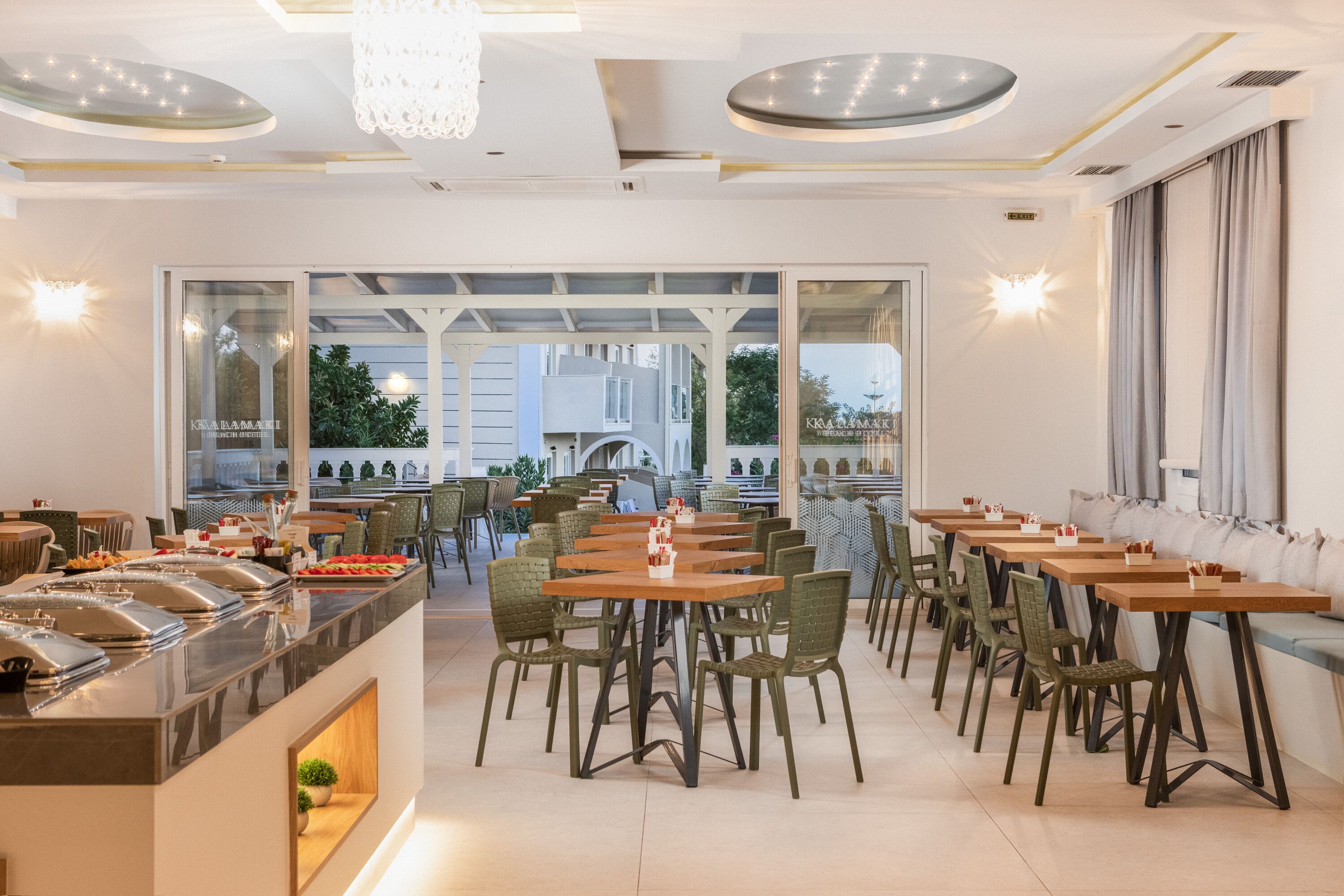 A modern dining area with multiple tables and chairs, a buffet counter, and large windows offering a view of the outdoors.
