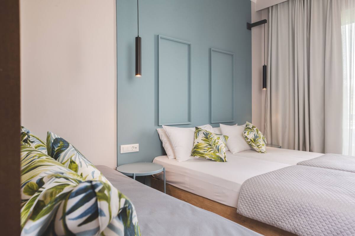 Une chambre d’hôtel avec un grand lit, une petite table ronde et un canapé à motifs tropicaux.