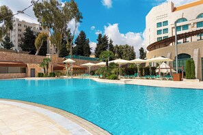 A swimming pool with lounge chairs and umbrellas, surrounded by a stone wall and trees. - Millennium Palestine Ramallah (Ramallah)