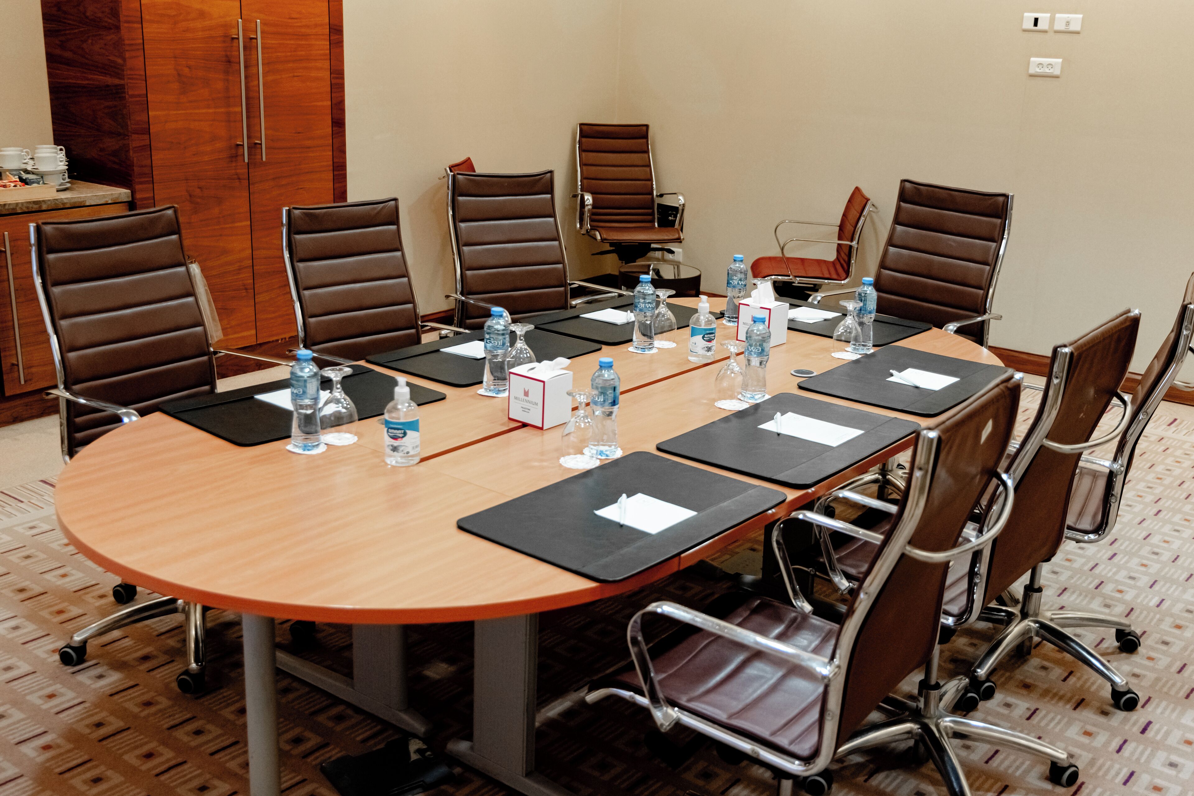 A conference room with a round table, brown leather chairs, water bottles, and nameplates.