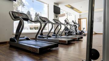 Un gimnasio con cintas de correr alineadas, ventanas amplias y piso de madera.