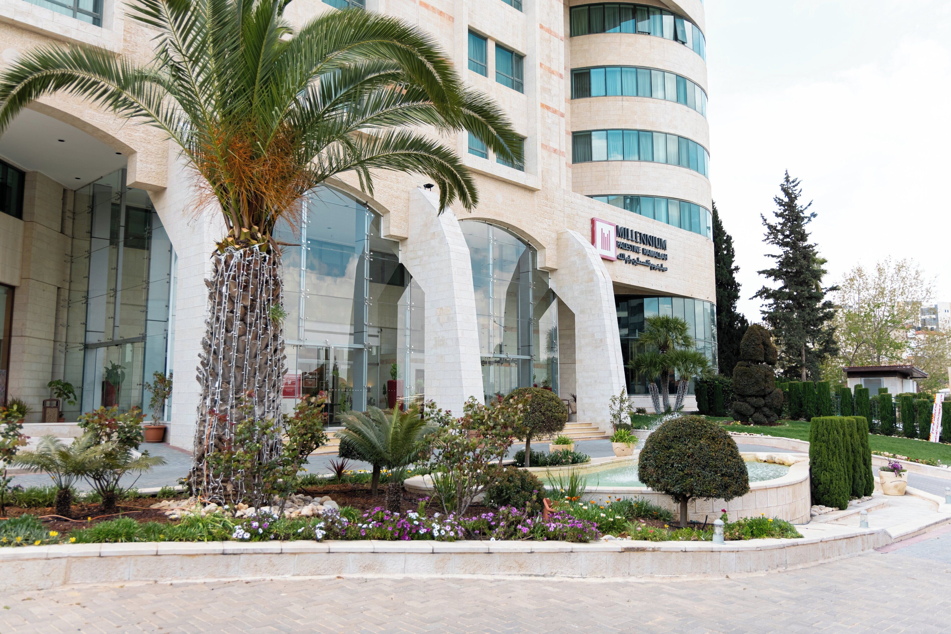 Un hotel moderno con un patio central que cuenta con palmeras, una fuente y diversas plantas.