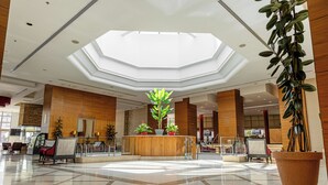 A spacious lobby with a central reception desk, large potted plants, and a high ceiling with skylights. - Millennium Palestine Ramallah (Ramallah)