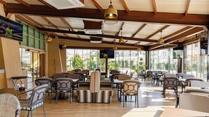 A spacious restaurant with wooden floors, striped cushioned seating, and large windows offering a view of the outdoors. - Millennium Palestine Ramallah (Ramallah)