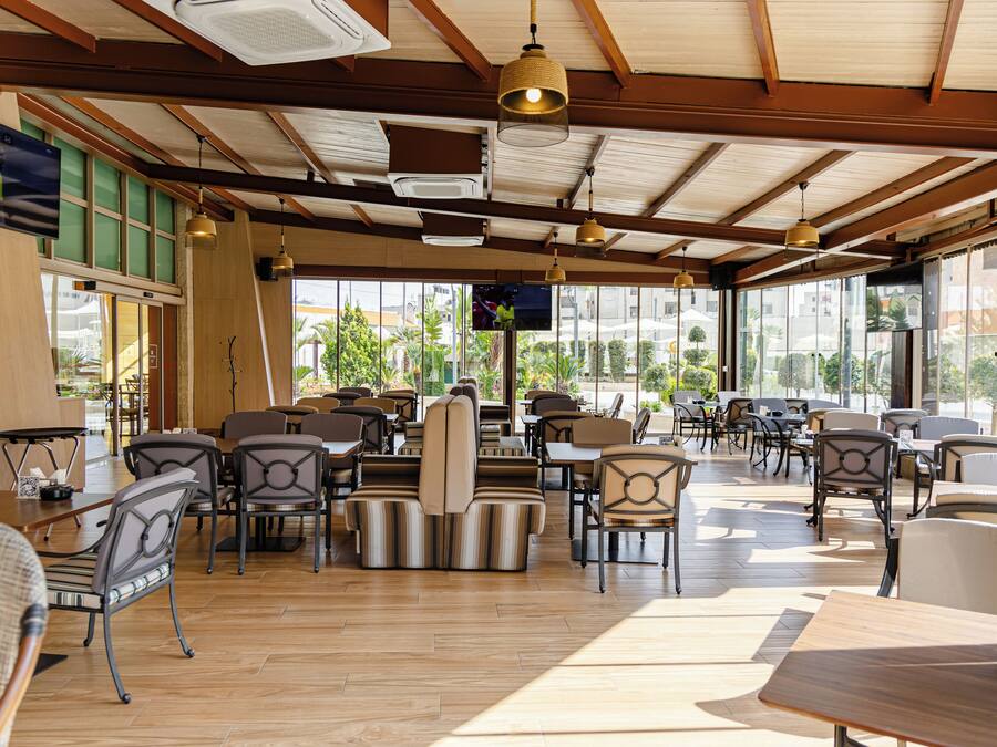 A spacious restaurant with wooden floors, striped cushioned seating, and large windows offering a view of the outdoors.