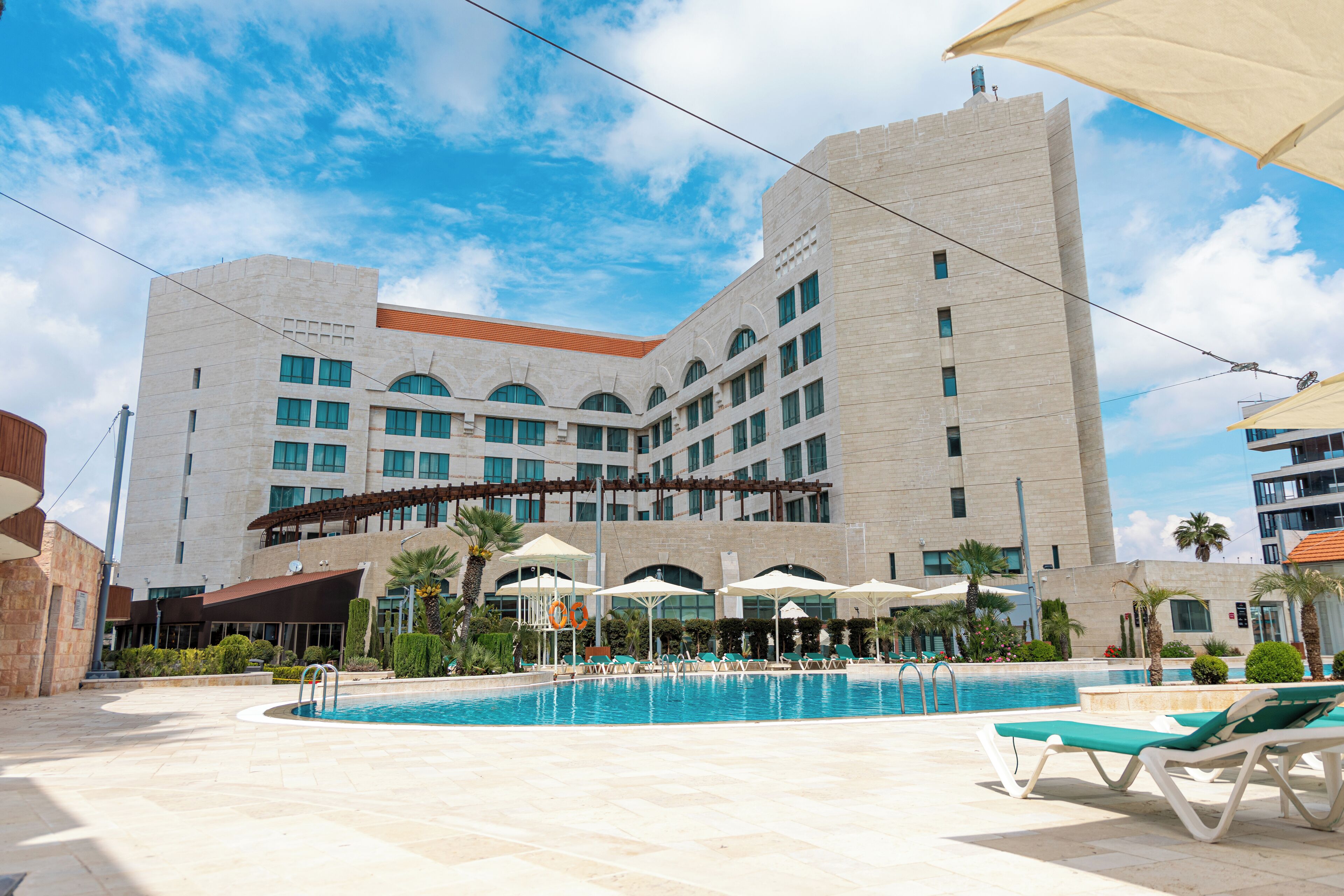 A hotel with a swimming pool, sun loungers, and umbrellas.
