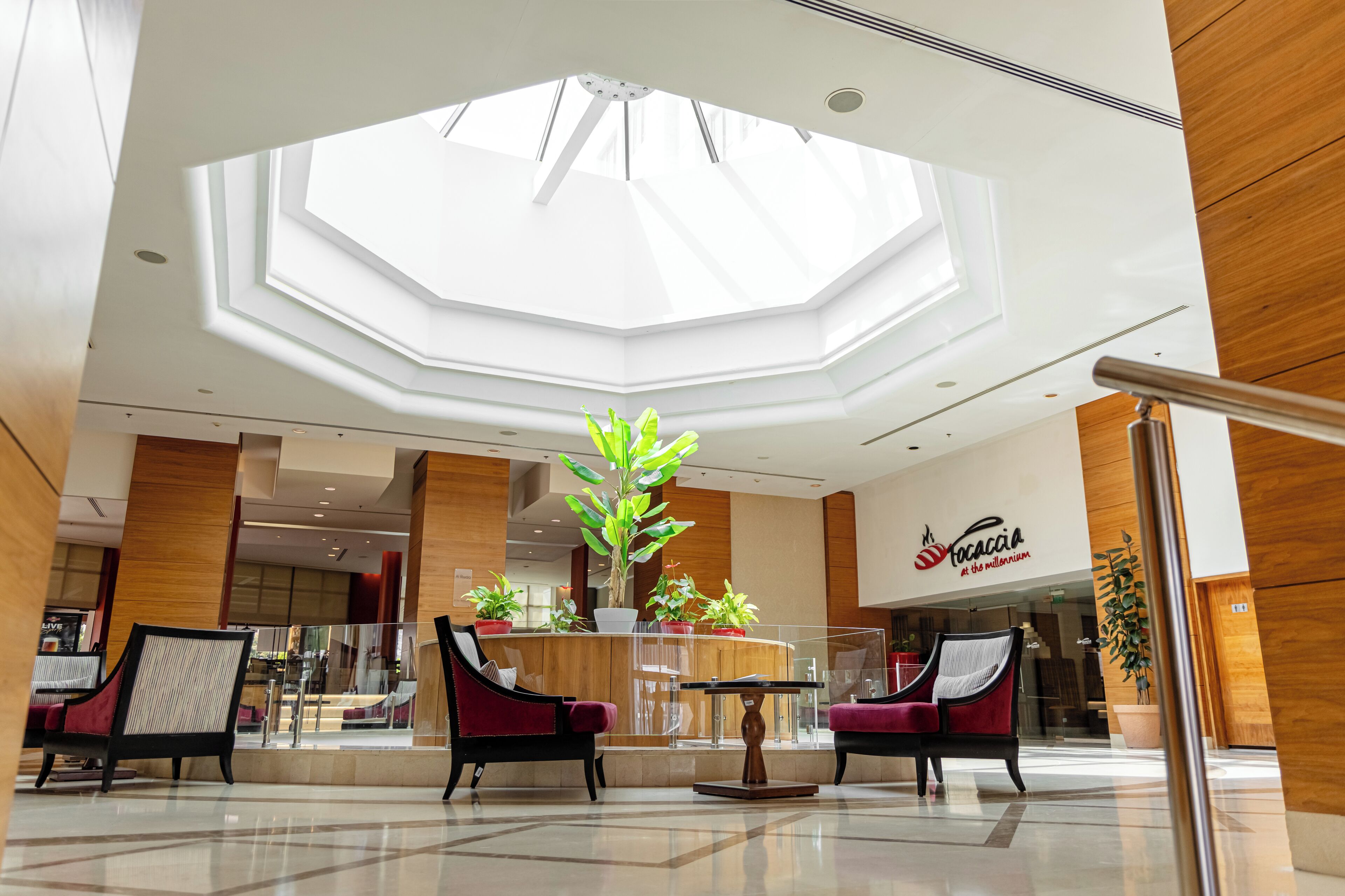 A hotel lobby with a central seating area, a large skylight, and a restaurant named "Tacacia."