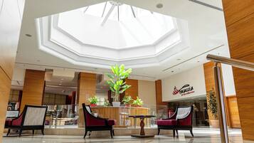 A hotel lobby with a central seating area, a large skylight, and a restaurant named "Tacacia."