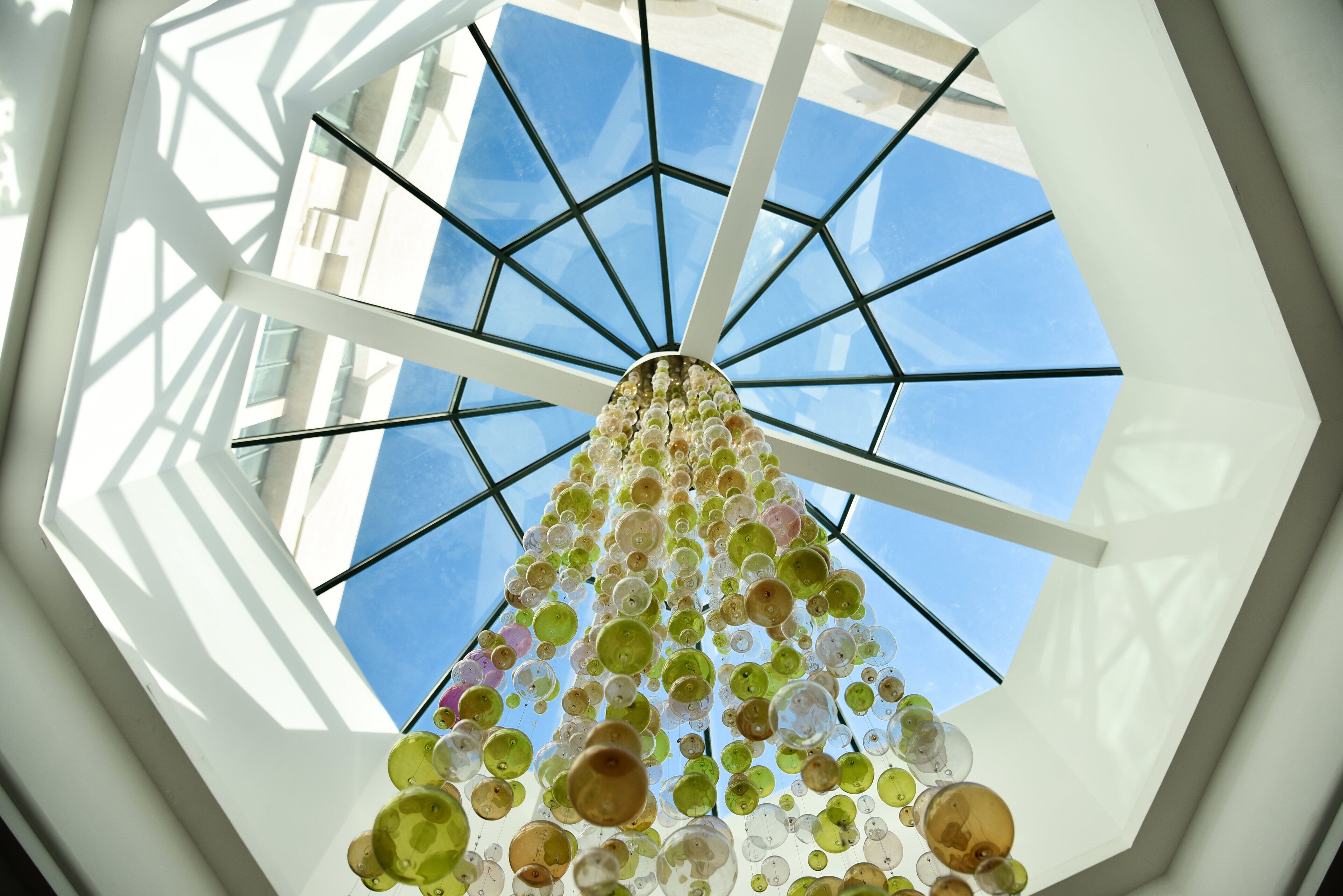 A ceiling with a geometric glass structure and hanging spherical objects.