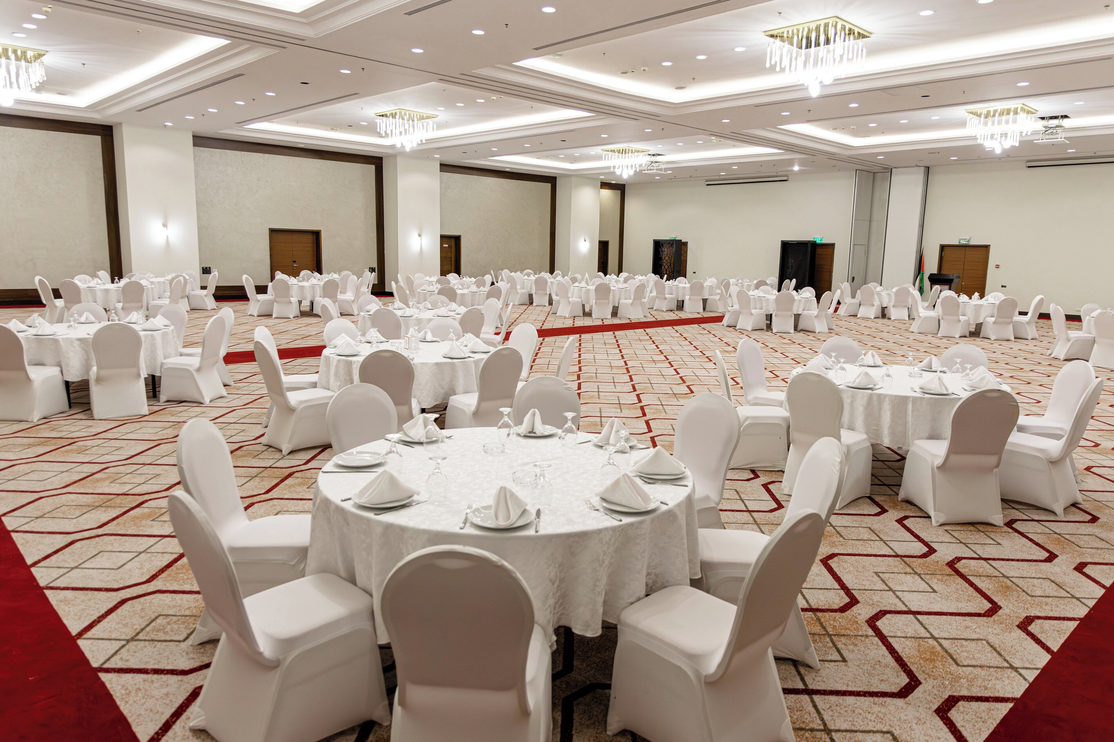 A large conference room with round tables and white chairs, carpeted floor, and chandeliers.