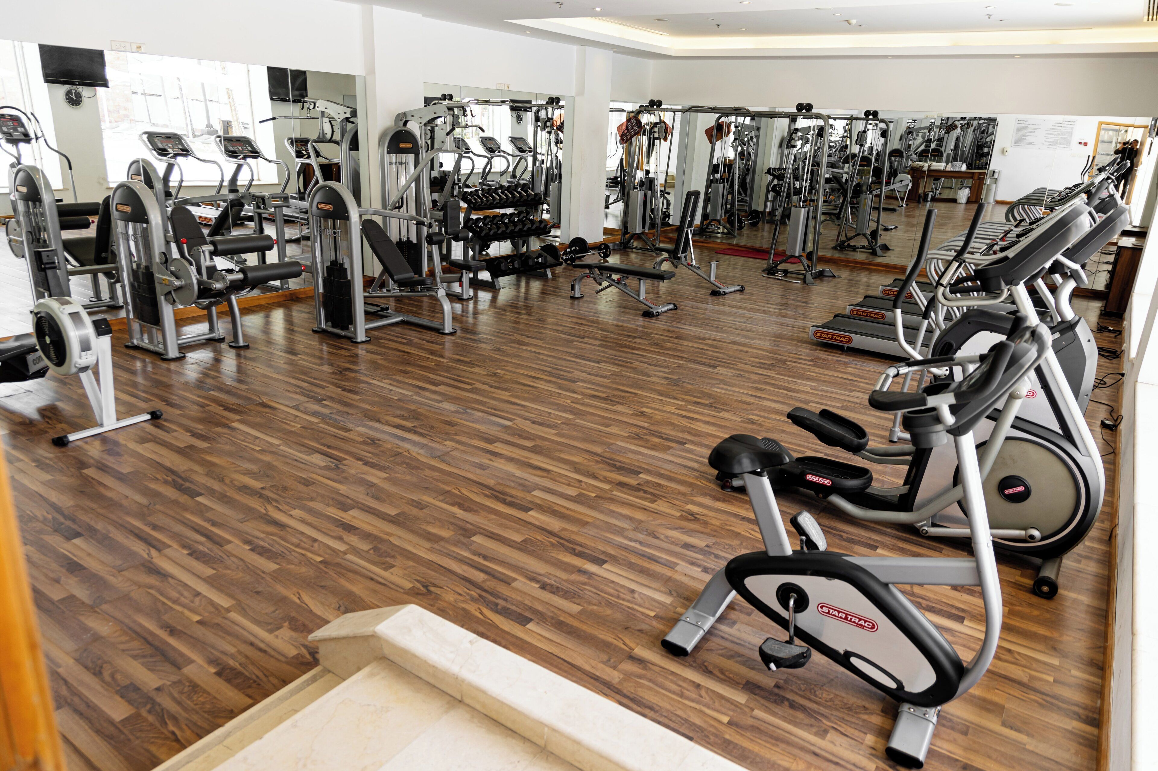 Ein Fitnessraum mit unterschiedlichen Trainingsgeräten, Holzböden und Spiegeln an den Wänden.