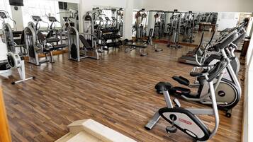 Ein Fitnessraum mit unterschiedlichen Trainingsgeräten, Holzböden und Spiegeln an den Wänden.