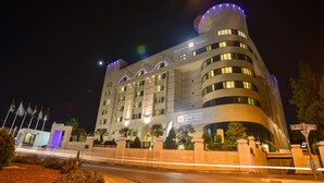 A modern hotel with a curved facade, multiple floors, and illuminated signage. - Millennium Palestine Ramallah (Ramallah)