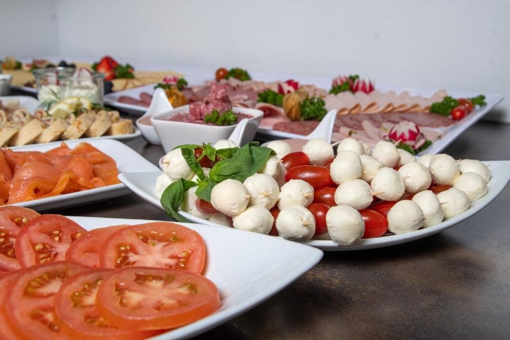Diversos tipos de alimentos, incluyendo tomates en rodajas, bolas de mozzarella, y diferentes tipos de carne y queso.