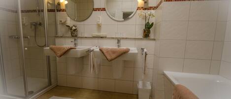 A modern bathroom with a glass-enclosed shower, two sinks, a bathtub, and a mirror above the sink.
