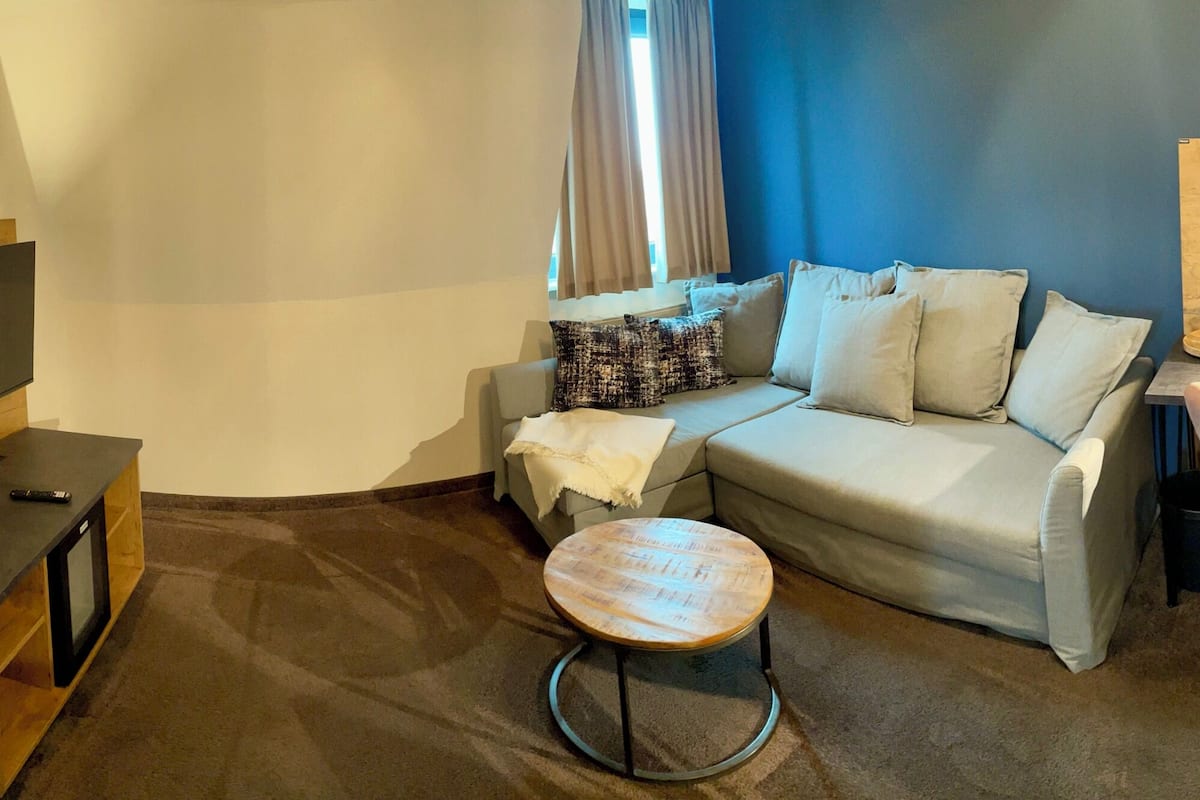 A hotel room with a bed, a TV, a sofa, a small round table, and a chair.