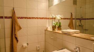 Un baño con inodoro, lavamanos y ducha. Hay toallas colgadas en la pared y un espejo sobre el lavamanos.