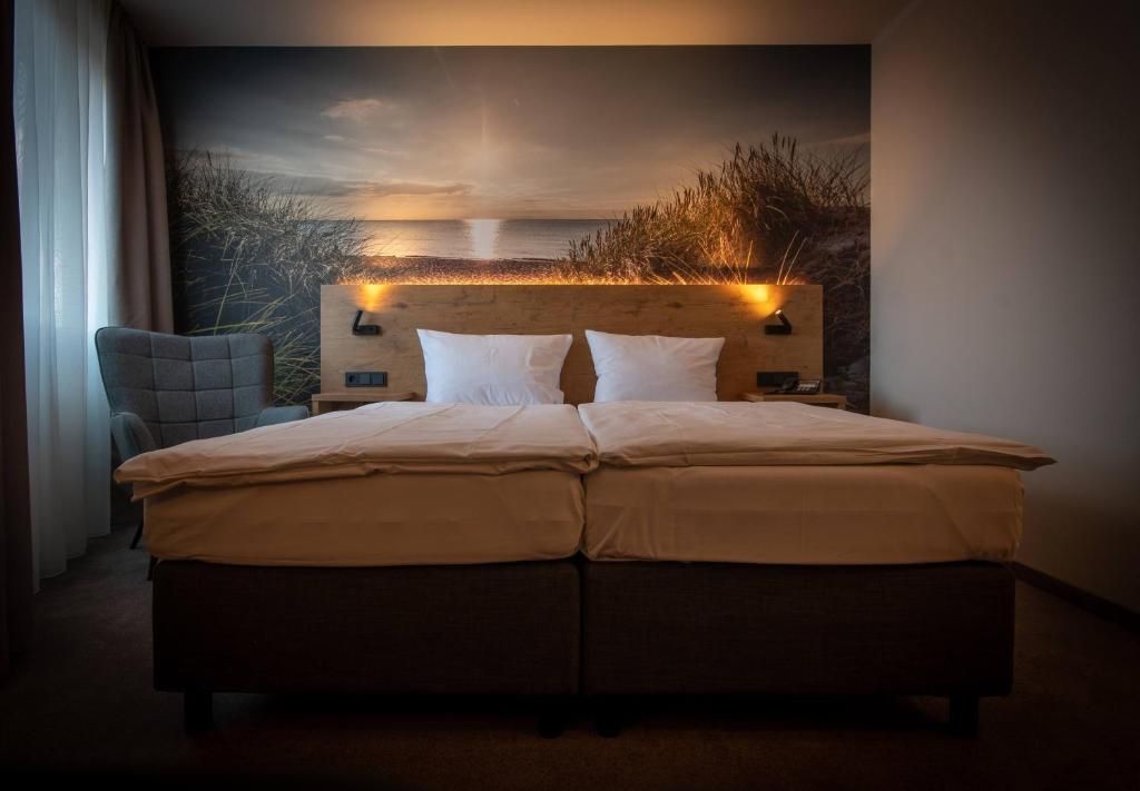 A double bed with a headboard against a wall, a chair to the left, and a view of a sunset over water.