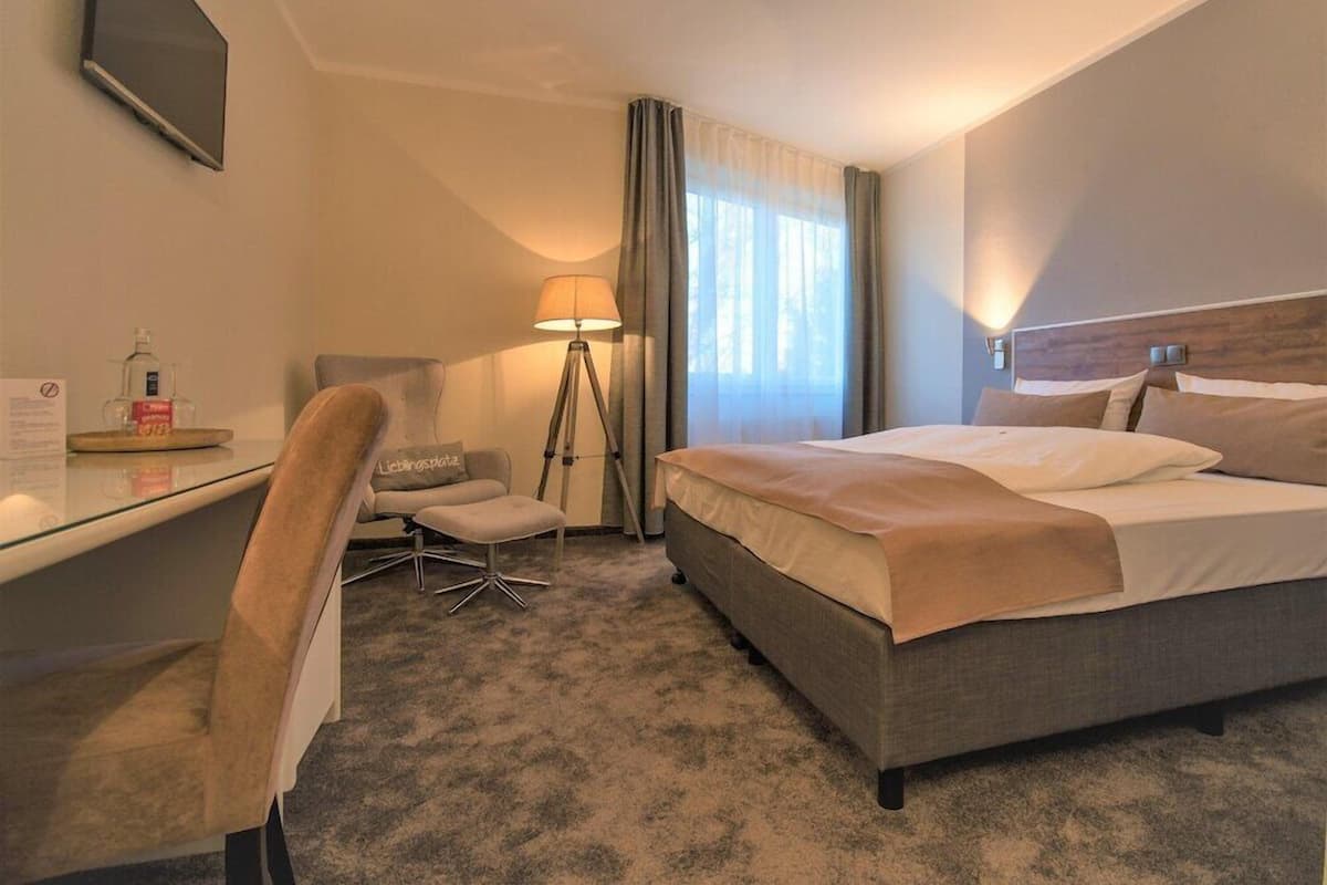 A hotel room with a bed, desk, chair, lamp, and curtains.