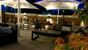 An outdoor seating area with tables and chairs, umbrellas, and potted plants. - Hotel Stadt Aurich (Aurich)