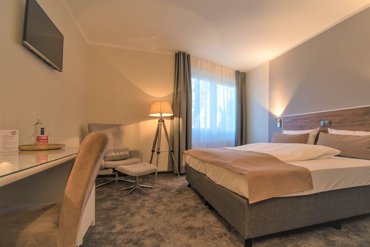 A hotel room with a bed, a desk, a chair, a lamp, and a window with curtains.