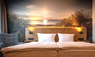 Habitación de hotel con cama, mesita de noche y cabecera, con vista al mar y al césped.