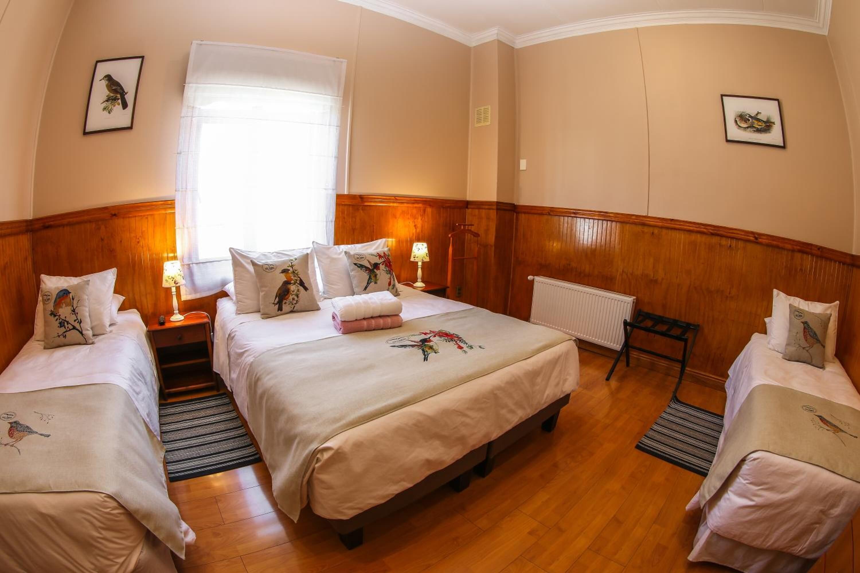 Una habitación de hotel con una cama grande, dos camas más pequeñas, suelo de madera y un radiador.