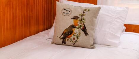 Una cama con almohada adornada con pájaros y flores, una colcha blanca y un cabecero de madera.