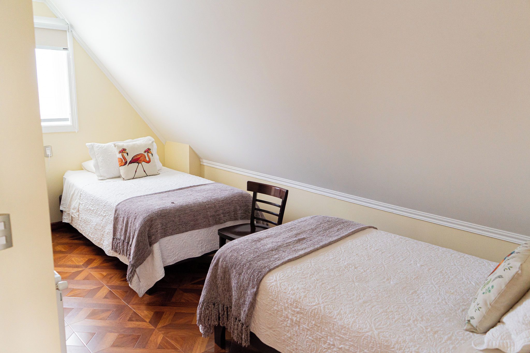 Un dormitorio con dos camas, una silla de madera y una ventana.