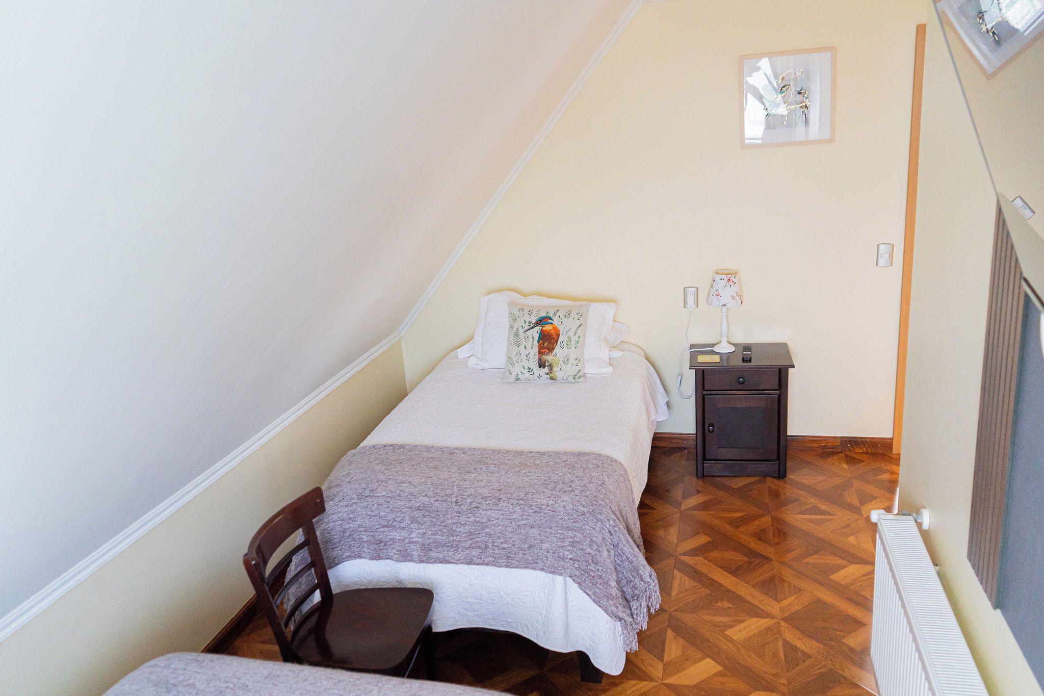 Een compacte, verzorgde slaapkamer met een enkel bed, een nachtkastje met een lamp en een stoel.