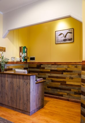 Un espace d’accueil avec un comptoir de réception en bois, un mur jaune et un tableau représentant une mouette.