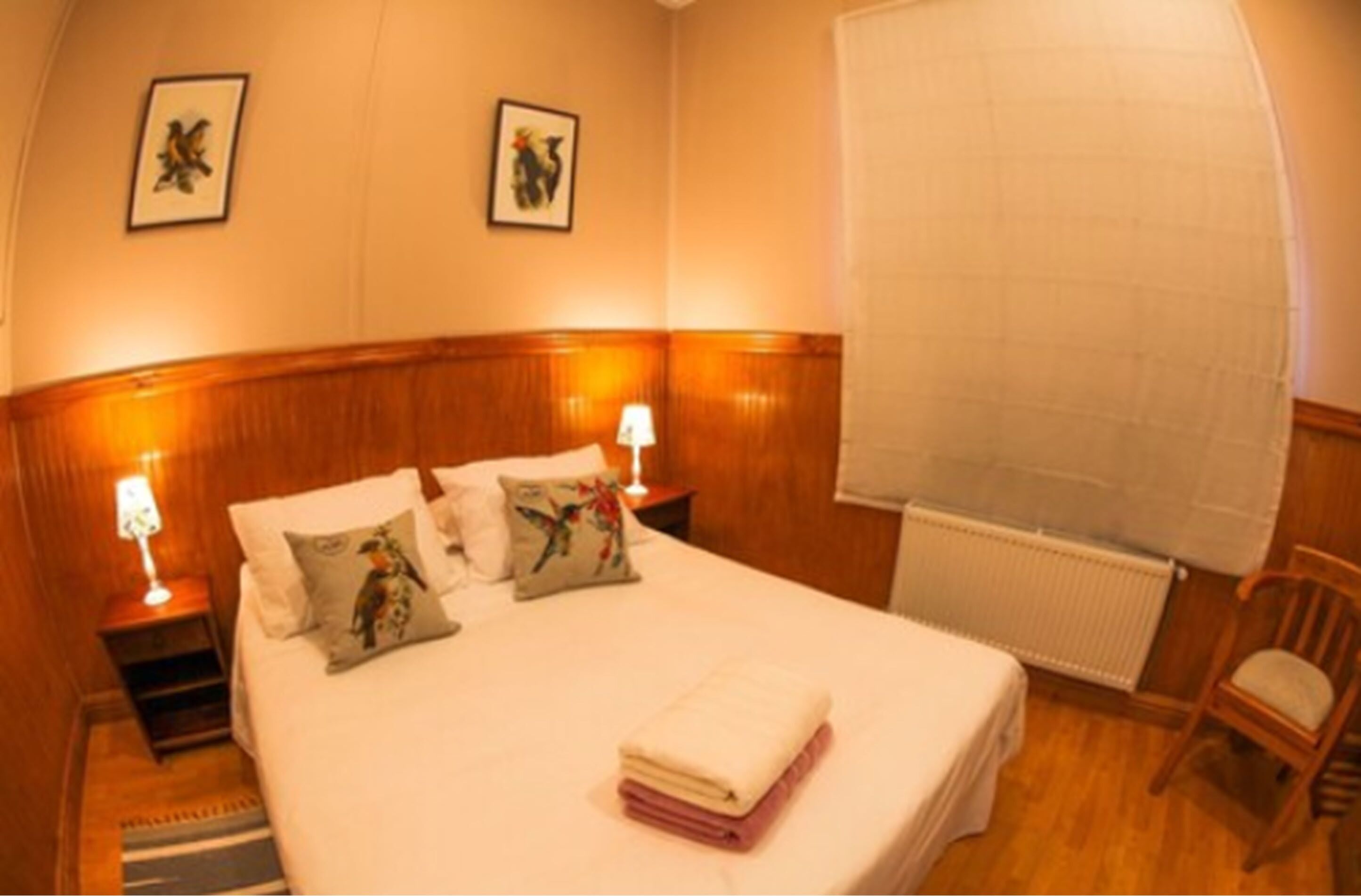 A hotel room with a large bed, two bedside lamps, a wooden headboard, and a radiator.