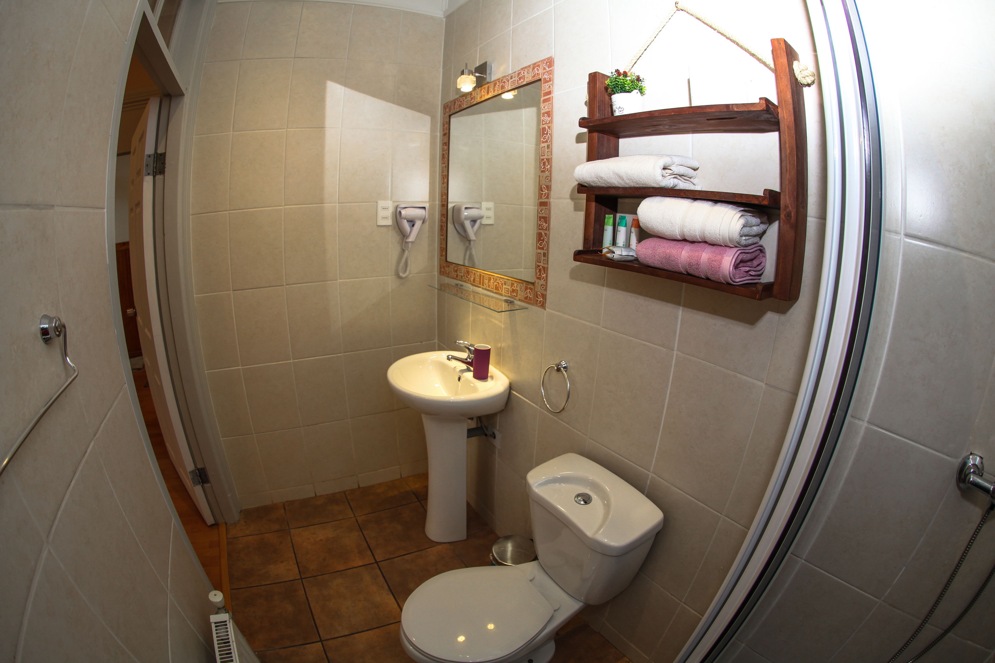A bathroom with a toilet, sink, and a mirror. There is a towel rack with towels and toiletries.