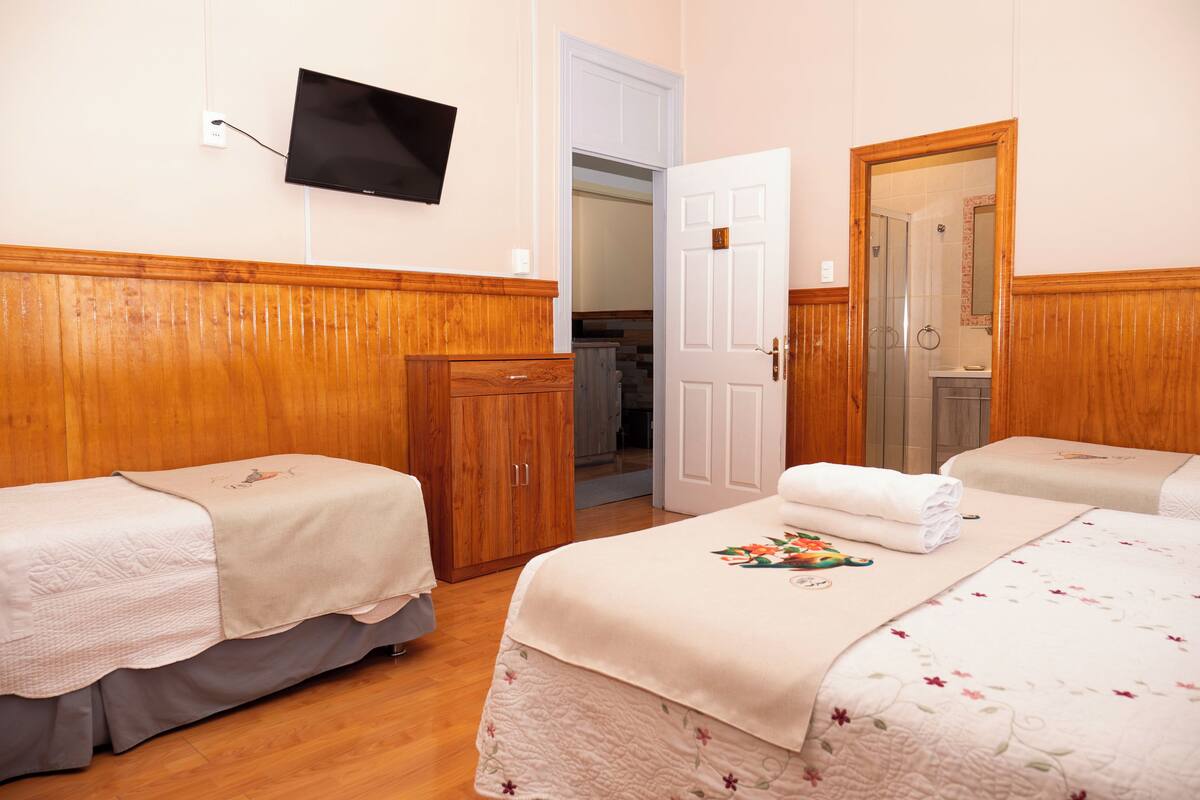 A hotel room with two beds, wooden paneling, a TV mounted on the wall, and a door leading to a bathroom.