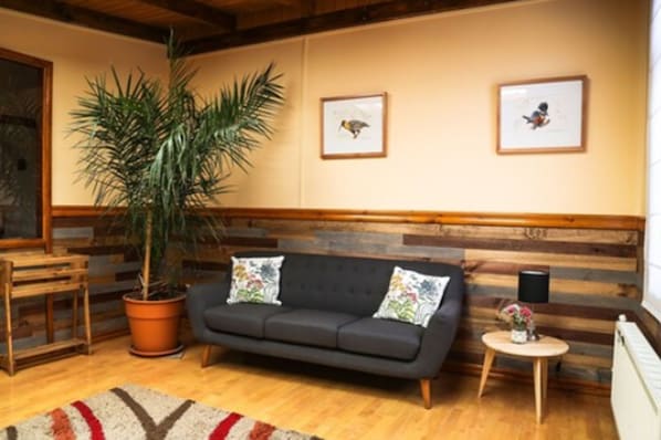 Un salon chaleureux avec un canapé foncé, une plante en pot et une petite table ronde surmontée d’une lampe.
