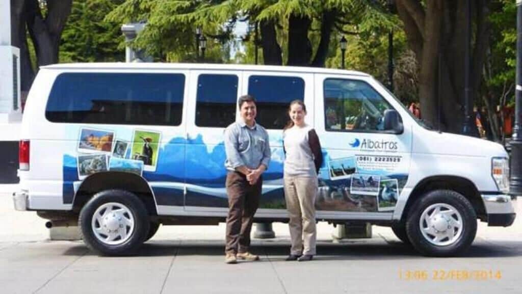 A white van with a blue and white design, parked on a sidewalk with two people standing beside it.