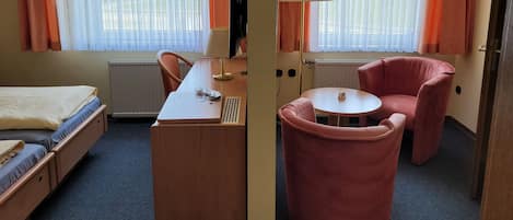 Quarto de hotel com cama, escrivaninha, cadeira, televisão e janelas com cortinas.