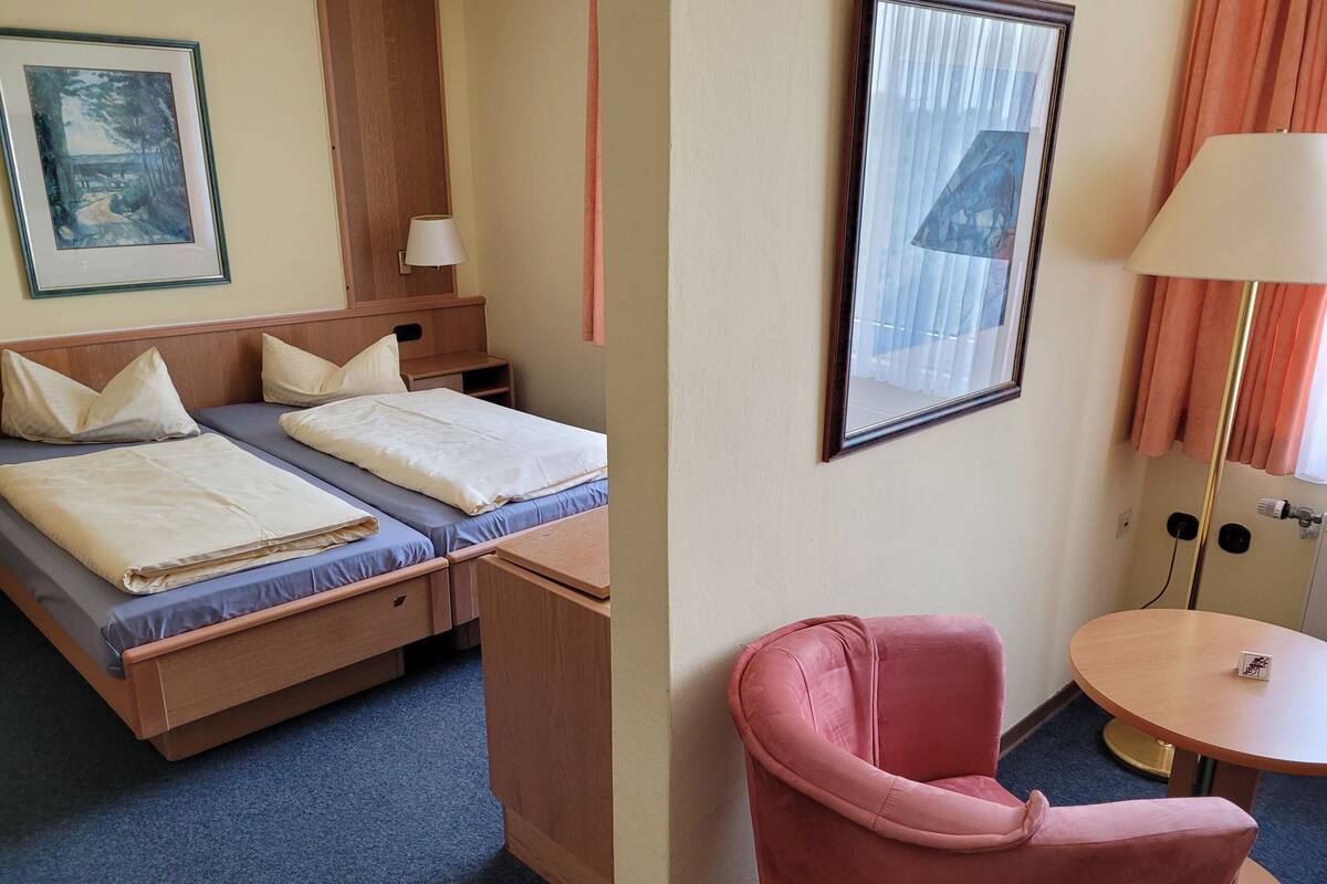 A hotel room with a bed, bedside tables, a desk, a chair, and a small table.