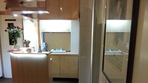 Eine kompakte Küche mit einer zentralen Kochinsel, einem kleinen Kühlschrank und einer Mikrowelle. Auf der Arbeitsplatte steht eine Vase mit Blumen, und auf der Insel befindet sich eine Schale mit Obst.
