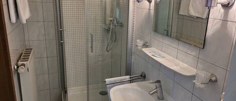 A modern bathroom with a glass-enclosed shower, a white sink, and a mirror with lights.
