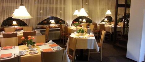 A dining area with tables set for service, chairs, hanging lamps, and a clock on the wall.
