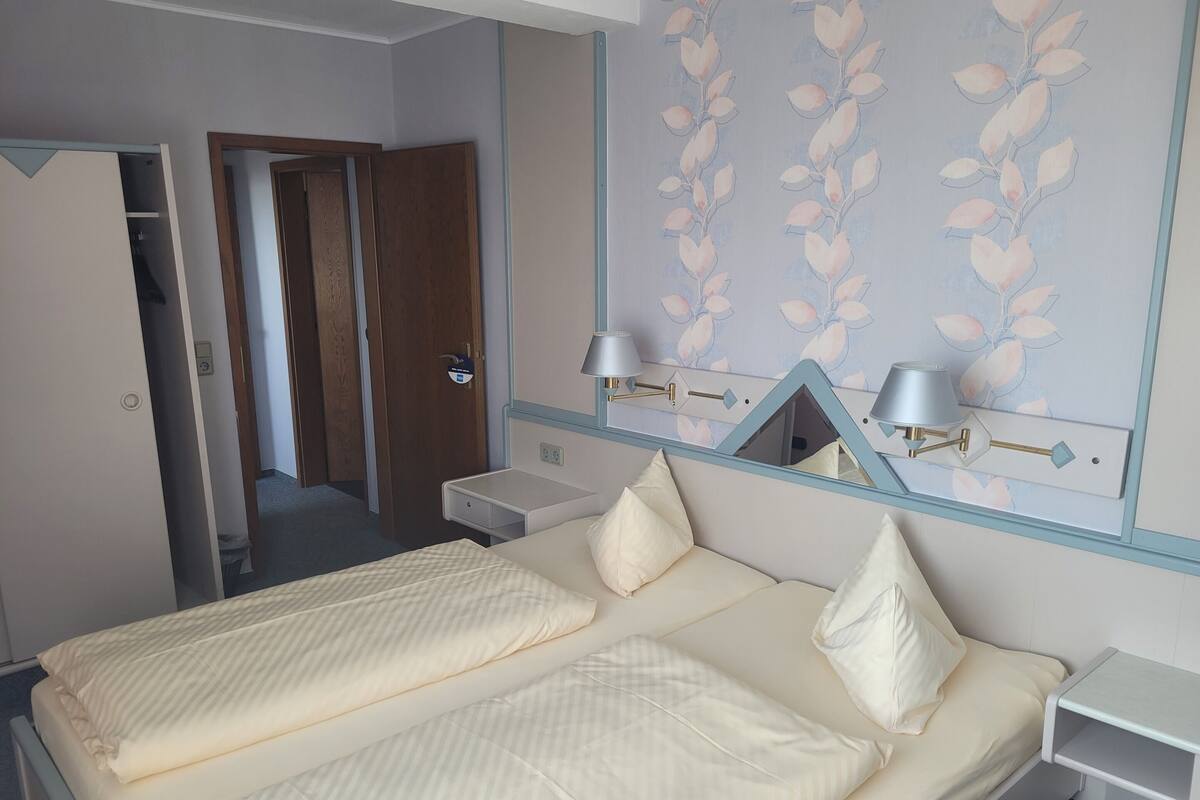 A hotel room with a bed, bedside tables, a mirror, and a door leading to a hallway.