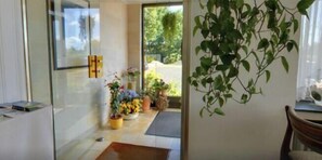 A modern interior with a glass door leading to an outdoor area, a wooden table with a vase of flowers, and a hanging plant. - EMS Hotel (Emden)